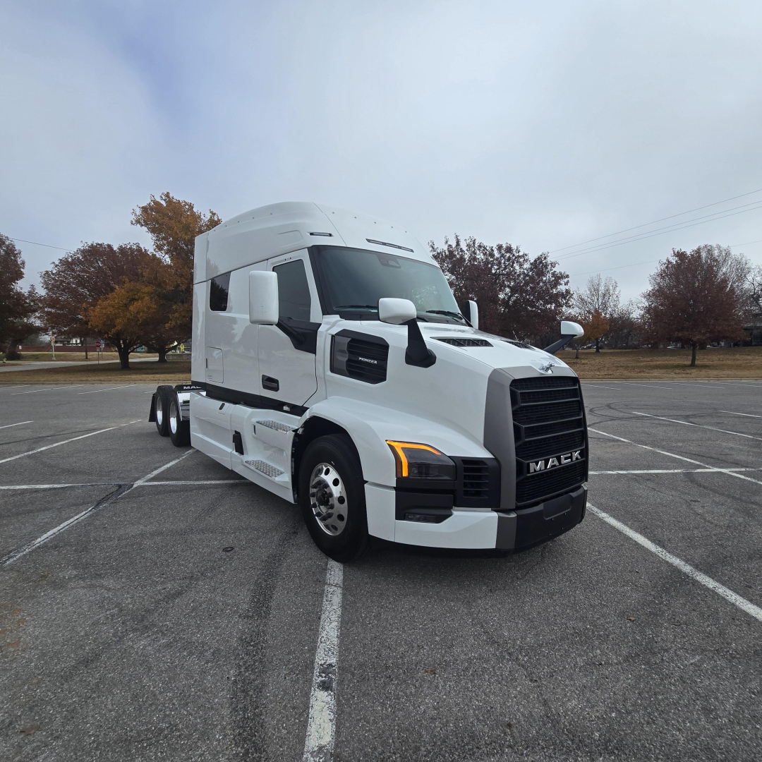 Truck cab with Mack PR64T76M branding on front grille. Side windows, white exterior, 18k+ front headlights. Text on image not visible except vehicle branding.