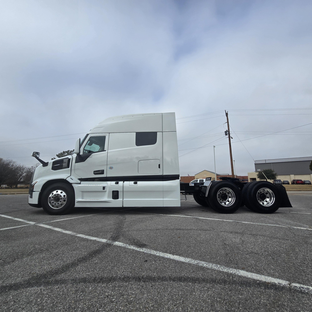 Truck side view of a white Mack PR64T76M conventional sleeper tractor showing a long cab and rear axle assemblies.