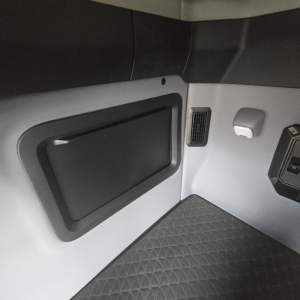 Trucker cab interior paneling with a storage hatch and ventilation vent on the side of a Mack PR64T76M truck interior.