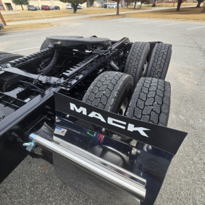 Truck chassis with dual rear axles and Mack logo plate on mudguard-view showing long chrome exhaust and suspension components.