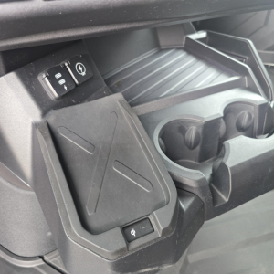 Inside cabin center console of a 2026 Mack PR64T76M showing cup holders, storage bin, and a small switch adjacent to a USB-like port.