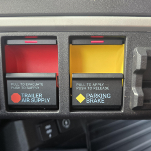Truck control panel showing trailer air supply and parking brake switches with red and yellow levers.