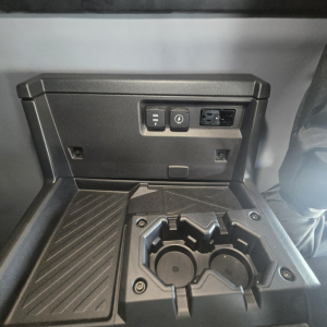 Dashboard area of a new Mack PR64T76M showing cupholders and control panel with 12V/USB ports and power outlet.