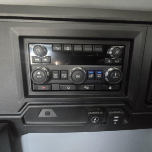 Dashboard control panel and USB/12V power outlet in Mack truck cab showing climate controls and media buttons.