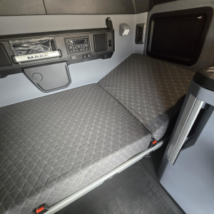 Interior of a Mack PR64T76M sleeper cab showing diamond-stitched seat/bed cushion, dashboard controls, and storage area.