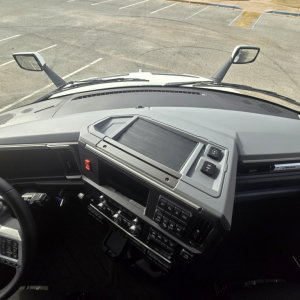 Mack PR64T76M truck interior dash view from driver seat showing center console touchscreen, steering wheel, and mirrors in foreground.