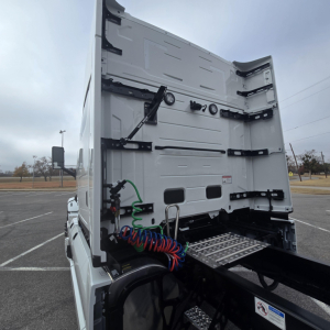 Truck rear view showing vertical tail area with fifth wheel and coiled air hoses, metal grab handles, and label stickers.