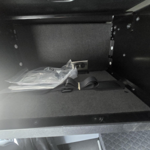 Cab interior storage drawer with strap and small plastic bag inside.