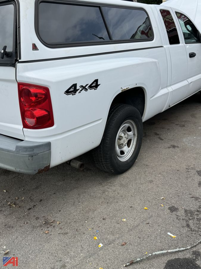 Dodge Dakota pickup truck with 4x4 badge on rear quarter panel, white crew cab with cap, visible rear wheel and taillight.