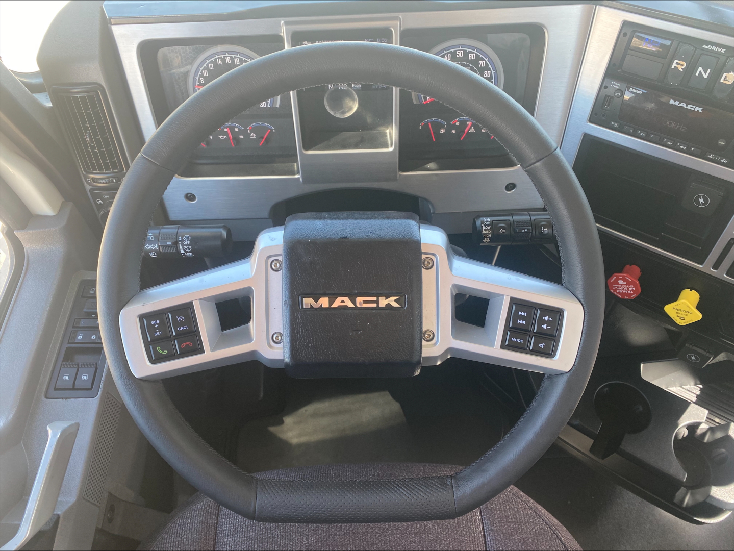 Mack AN64T truck interior steering wheel and dashboard, multiple gauges, control stalks, and Mack logo on steering wheel hub.