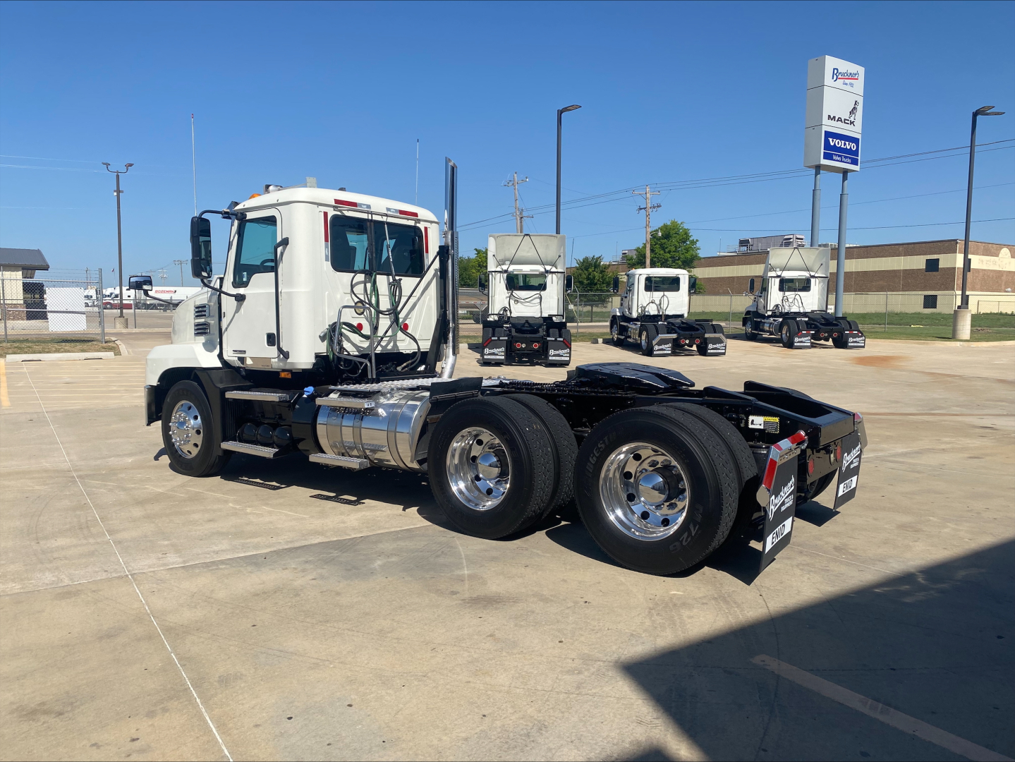 Truck chassis showing triple rear axles and white cab of a Mack AN64T daycab in a dealer lot.