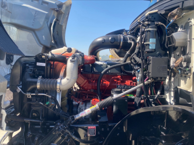 Mack AN64T engine bay showing red diesel engine, hoses, and surrounding components inside open hood.