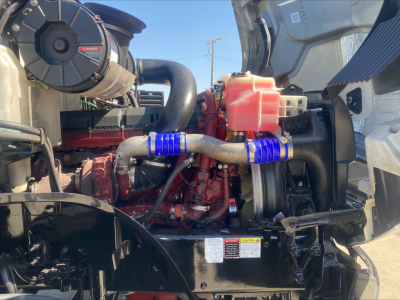 Mack AN64T engine bay showing radiator hoses, coolant reservoir, and engine components with blue hose sleeves.