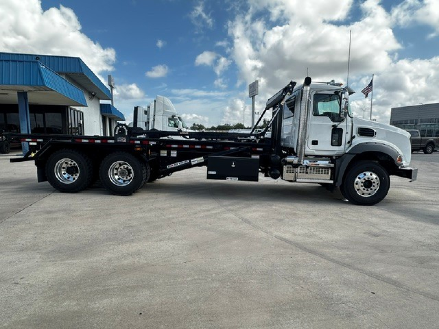 2026 Mack GR64B rolloff truck side view showing cab, long wheelbase chassis, and flatbed with twin rear axles.