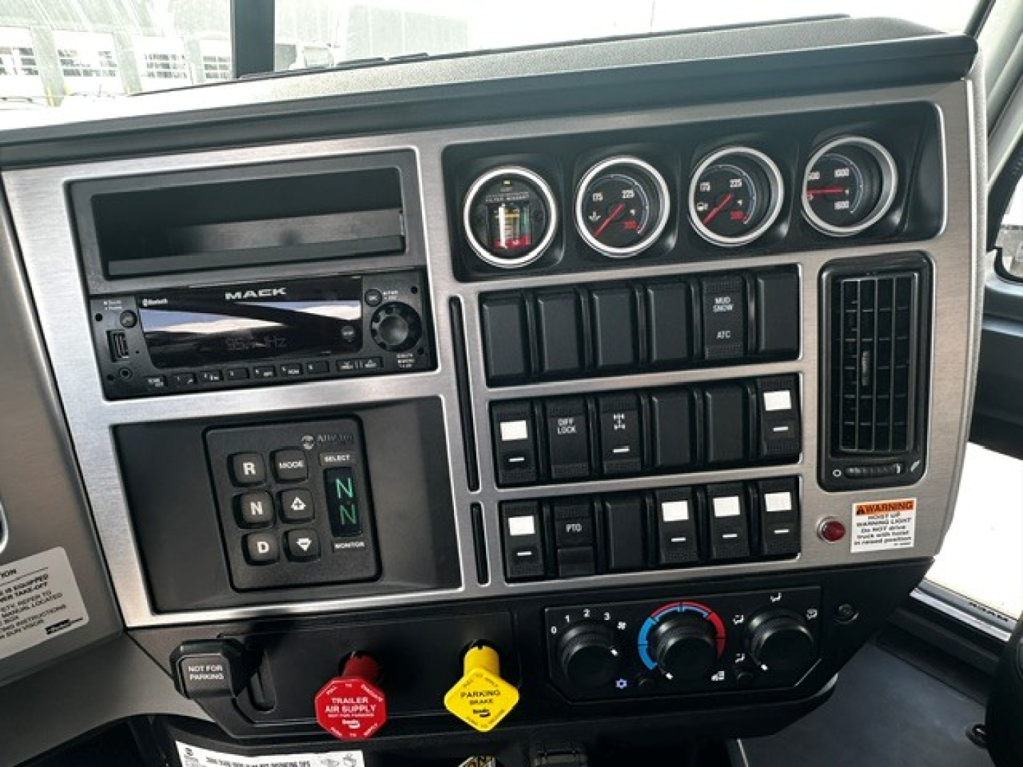 Dashboard panel of a 2026 Mack GR64B turnout showing multiple gauges, switches, and controls in a truck cab.
