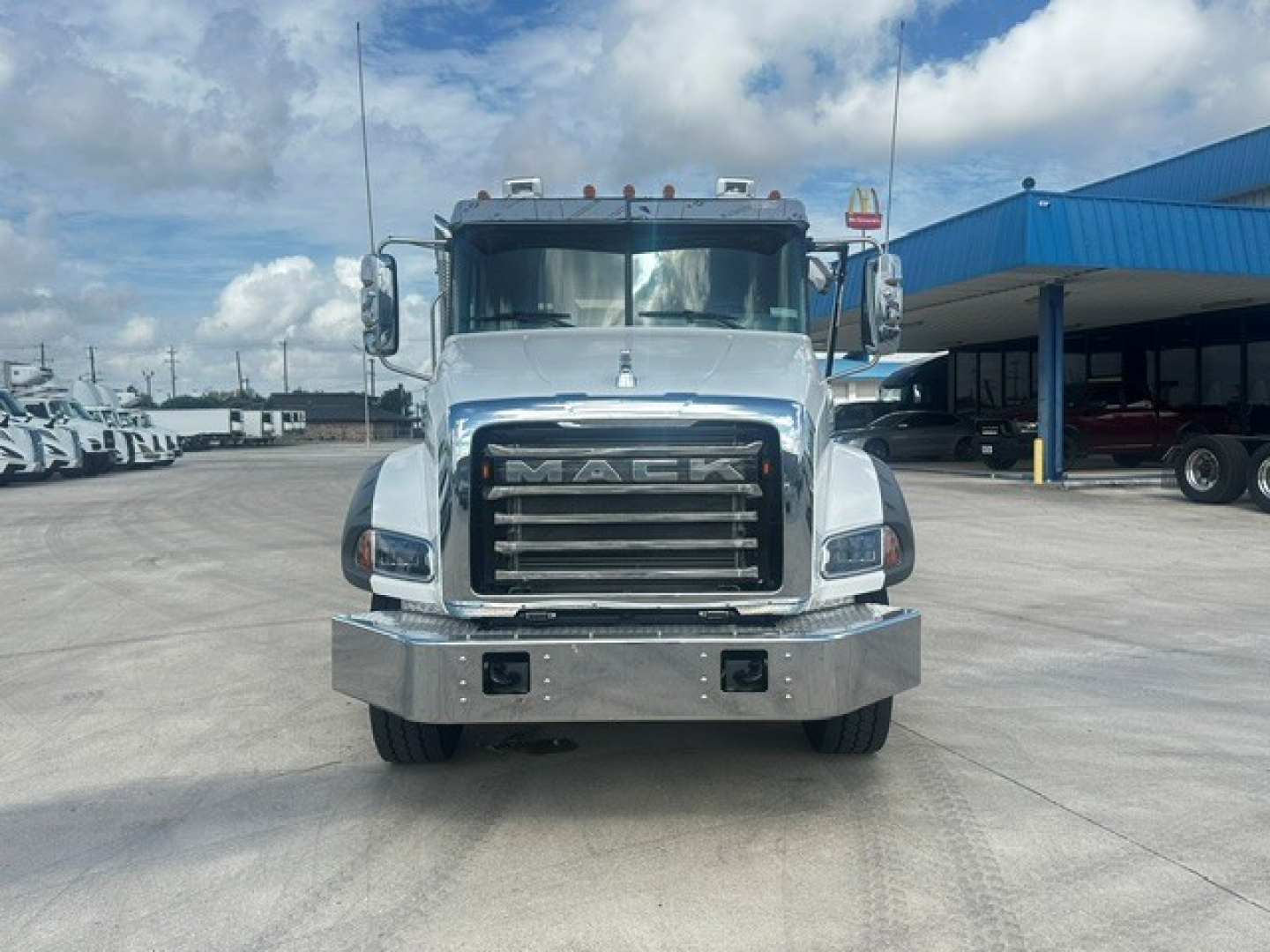 Front view of a new 2026 Mack GR64B rolloff truck showing chrome grille with M A C K letters, large bumper with two rectangular lights, and silver metallic body.