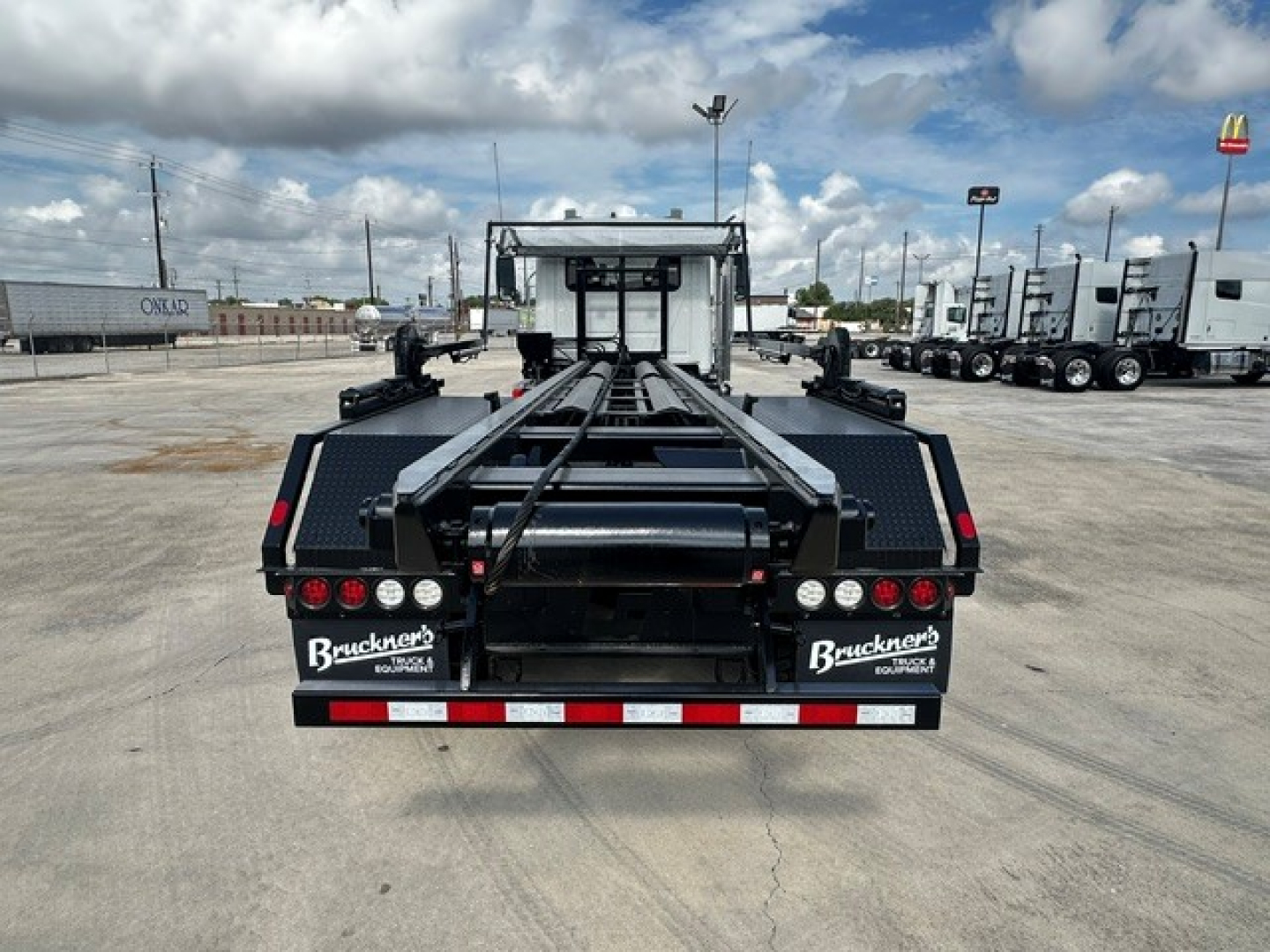 Truck chassis view from rear showing roll-off body frame and stacked hydraulic components, Mack GR64B, new with stock 70090, VIN 1M2GR2GC0TM053340.