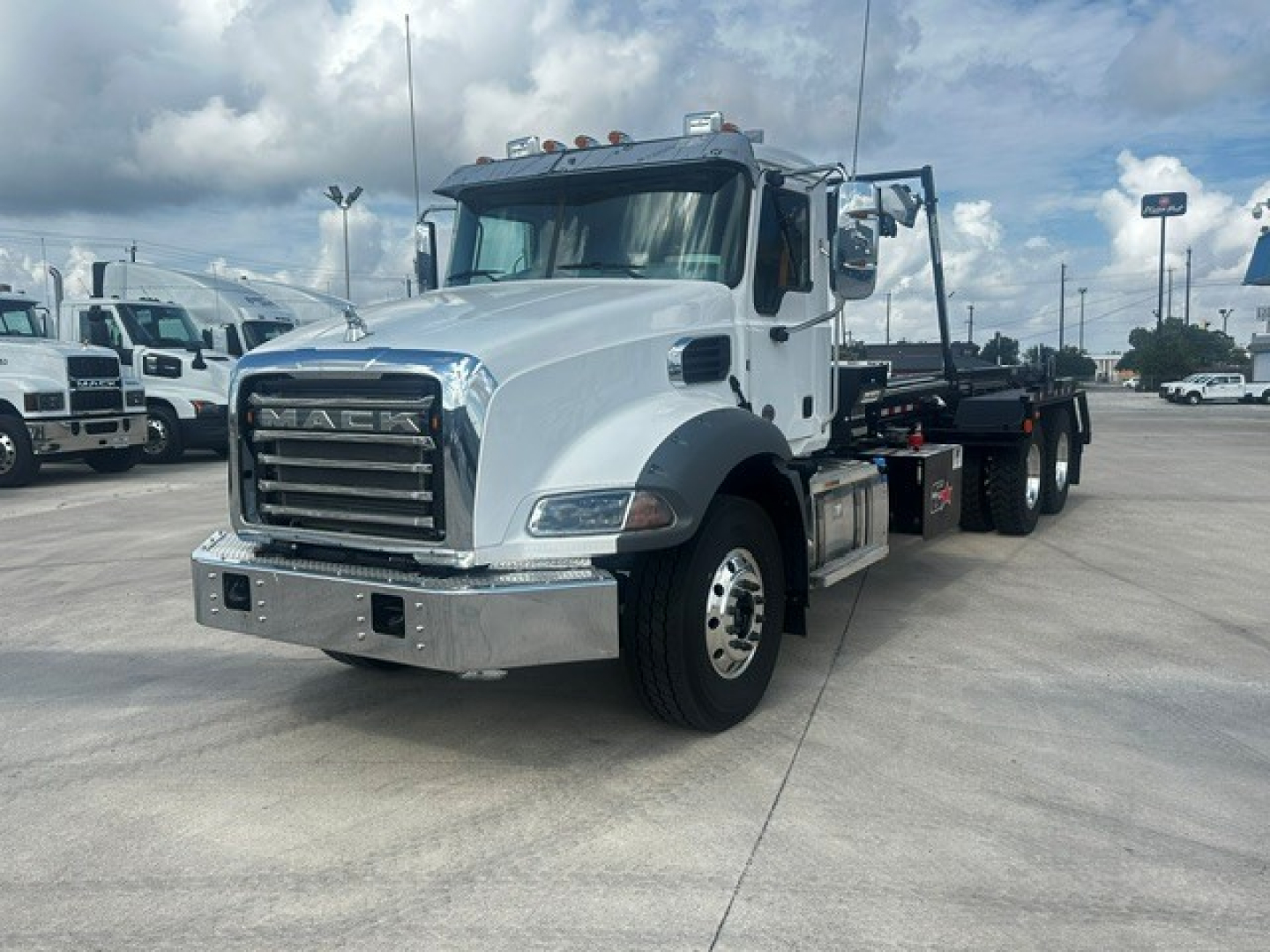 Mack GR64B roll-off truck in white with chrome bumper and grille, side view showing front wheels, cab, and chassis for a roll-off body.