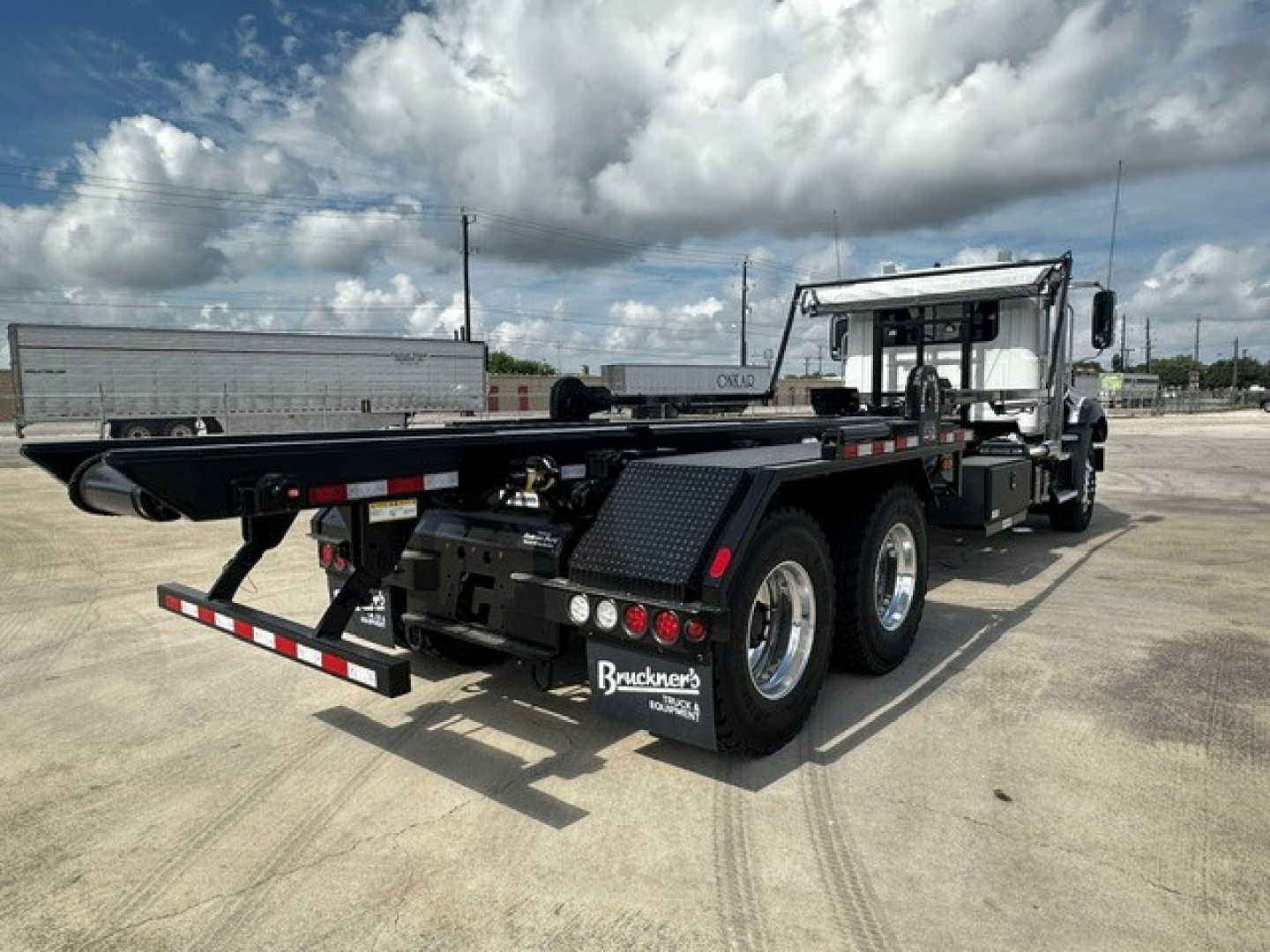 Mack GR64B roll-off truck rear view showing chassis and dual rear axles with black flatbed, taillights, and side guards.