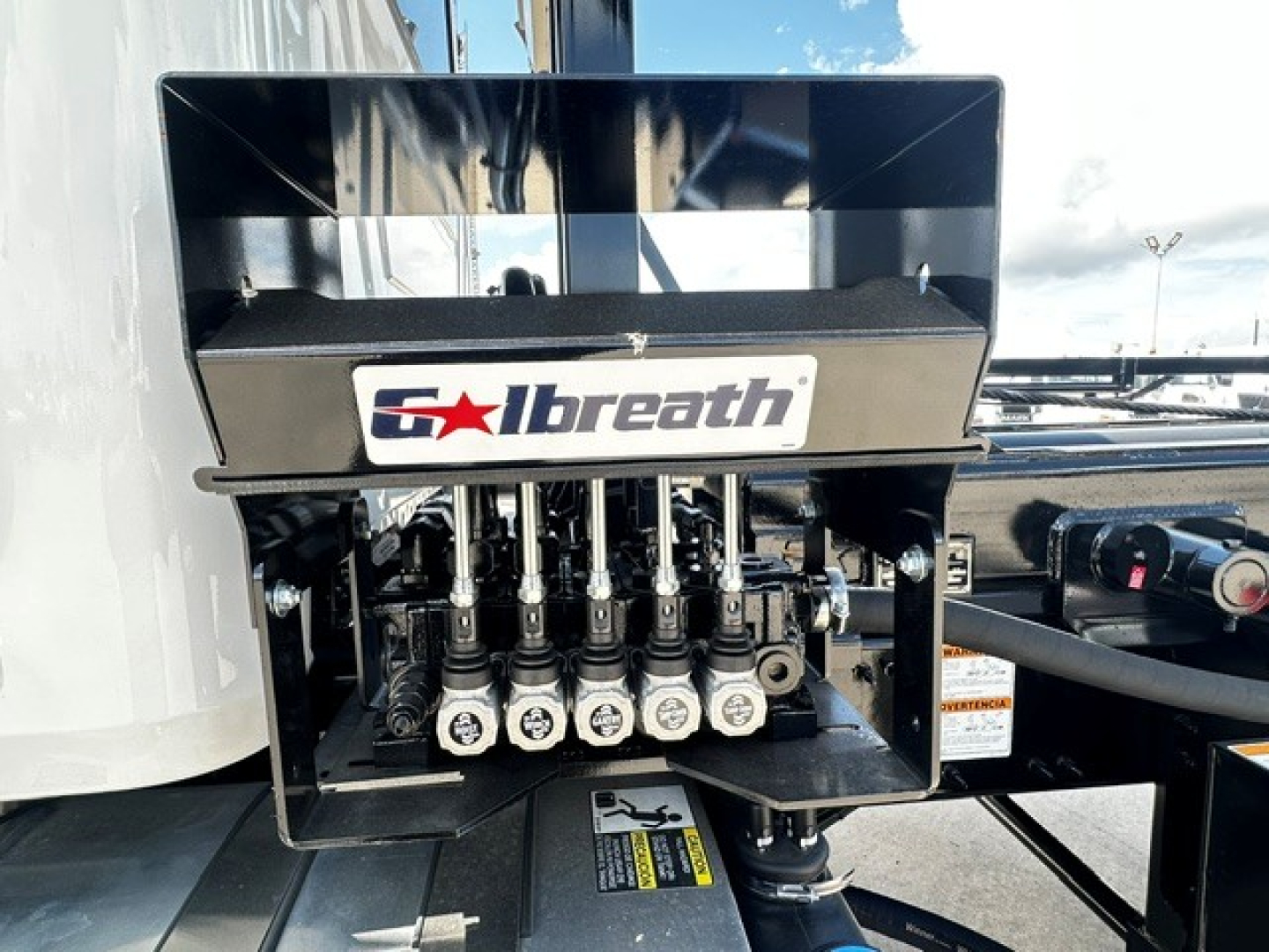 Valve manifold with multiple hydraulic lines and an 'Solbreath' logo on the equipment in a Mack GR64B roll-off truck photo.