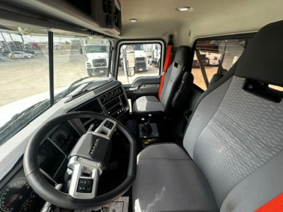 Mack GR64B truck cab interior showing steering wheel with Mack emblem, dashboard, and gray patterned seats; driver and passenger seats visible with large side windows.