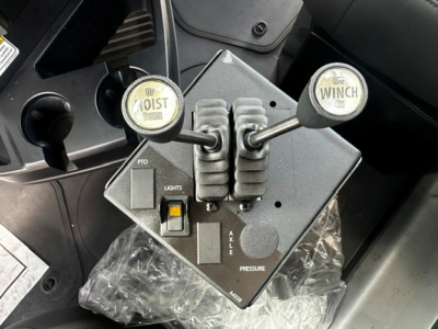 Mack GR64B control pedestal with levers labeled UP/DOWN and WINCH, showing PTO, LIGHTS switch, and AXLE/PRESSURE indicators.