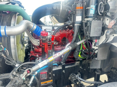 Mack GR64B engine bay showing red engine, green coolant hose, and various hoses and electrical wiring.