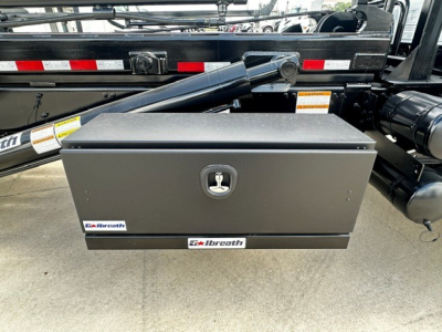 Box-shaped toolbox mounted on a Mack GR64B roll-off truck with two latches and brand stickers reading 'galbreath' or 'glbreath'? It shows a black metal toolbox with a central handle and two stickers on the front.