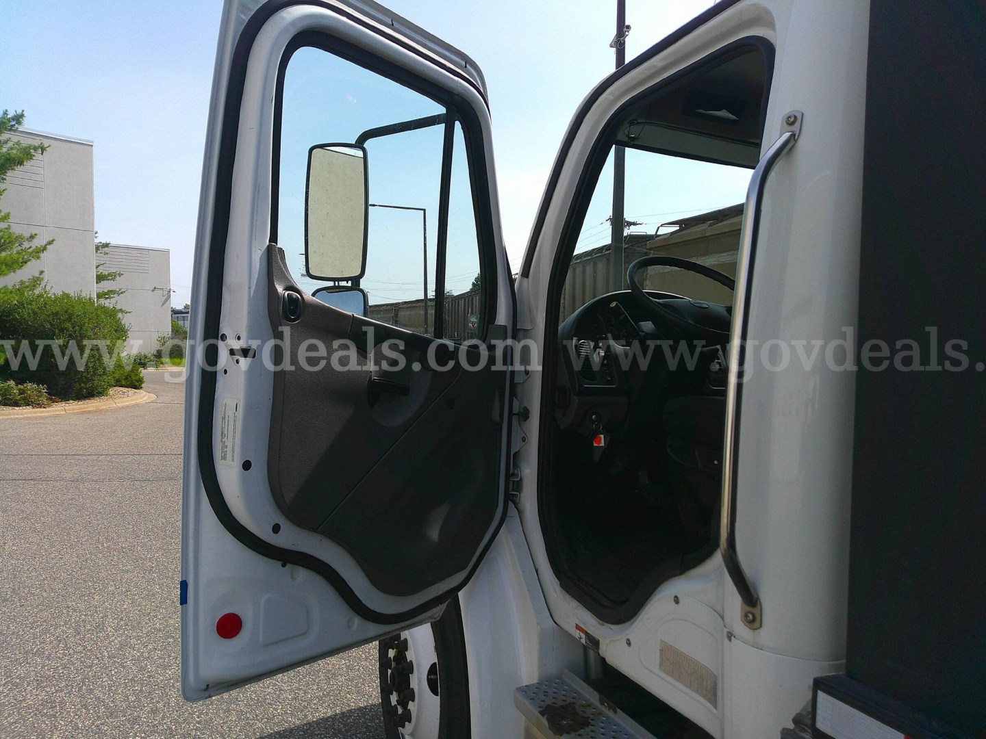 Truck cab interior and open door of a 2018 Freightliner M2-106 service/utility truck showing driver seat and dashboard area.