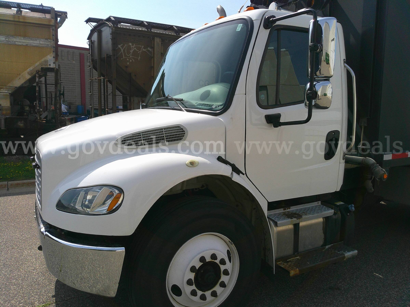 Freightliner M2-106 cab with white exterior, side steps, and dual rear wheels visible from passenger side; curbside view.