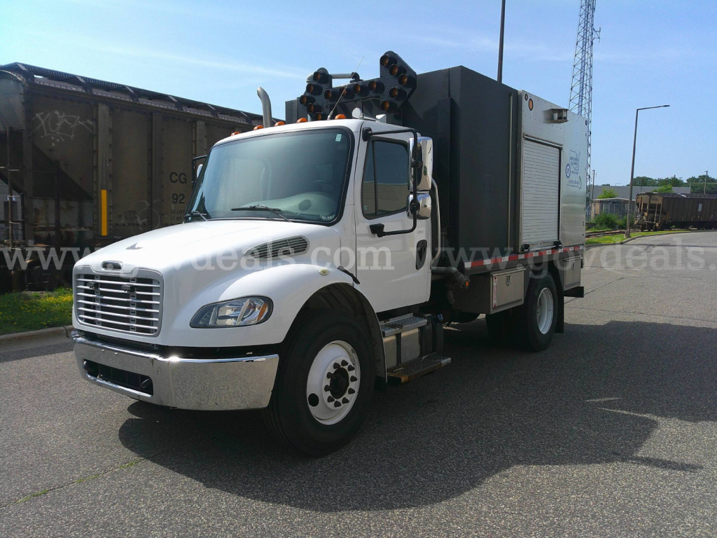 Truck engine bay area showing Freightliner M2-106 utility service body with mounted equipment and cab side view.