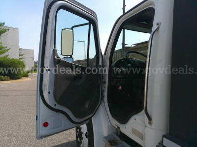Truck cab interior and open door of a 2018 Freightliner M2-106 service/utility truck showing driver seat and dashboard area.