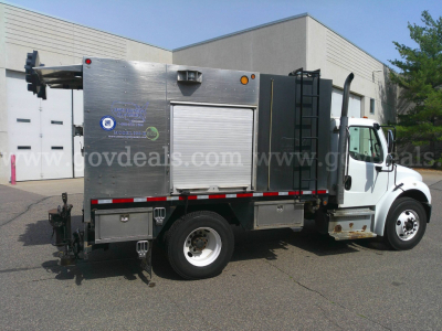 Truck side view of a service/utility Freightliner M2-106 with a metal utility box, roll-up door, ladder rack, and various decals.