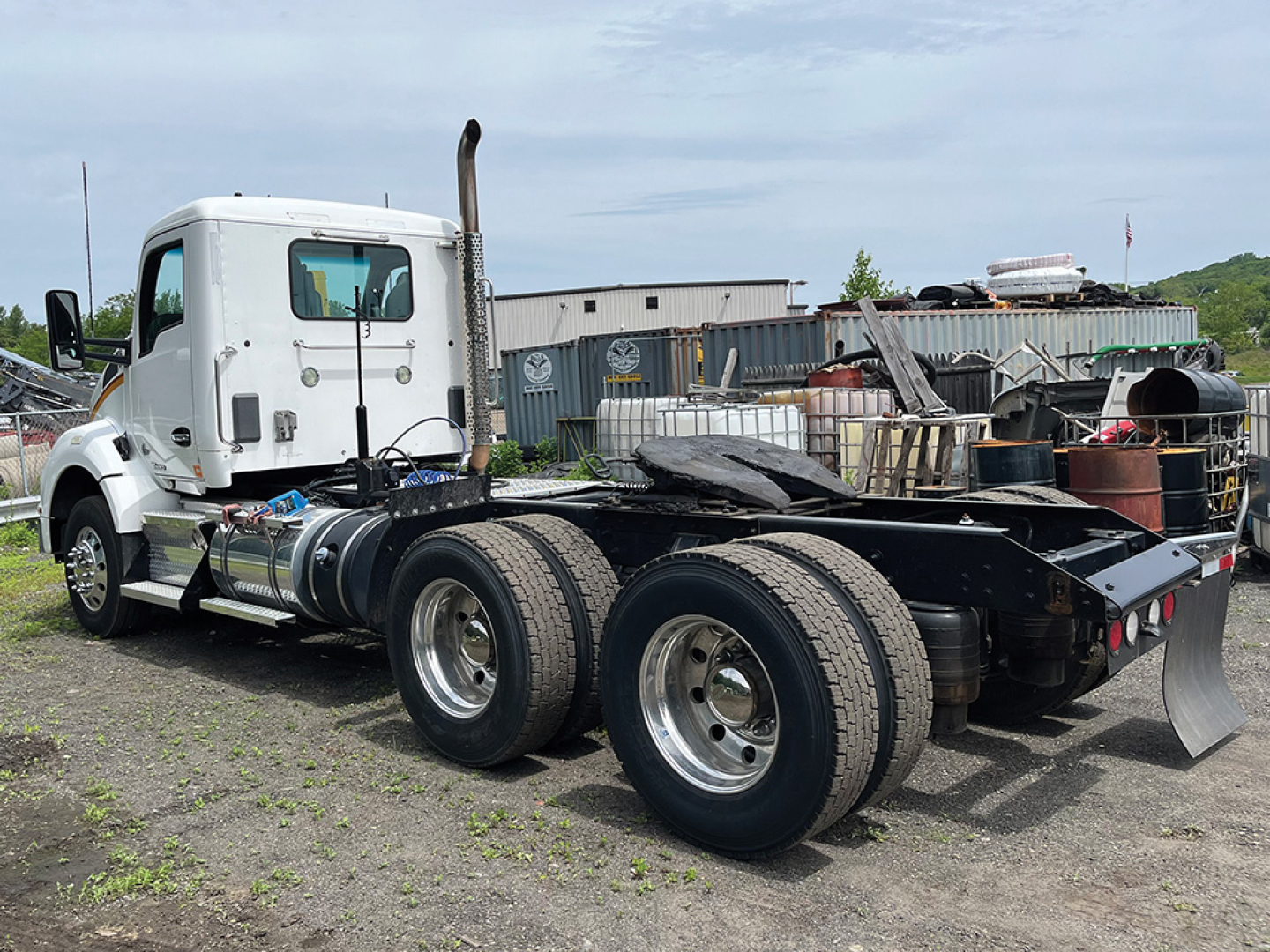 Kenworth T-880 tractor chassis rear view with dual rear axles and white cab, fuel tanks, exhaust stack visible.