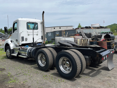 Kenworth T-880 tractor chassis rear view with dual rear axles and white cab, fuel tanks, exhaust stack visible.