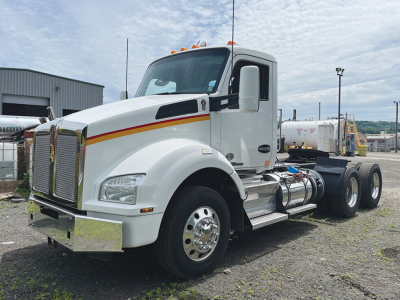 Kenworth T-880 conventional daycab truck in white with chrome bumper, grille, and dual rear axles. Side shows fuel tanks and steps; headlights and amber clearance lights visible.