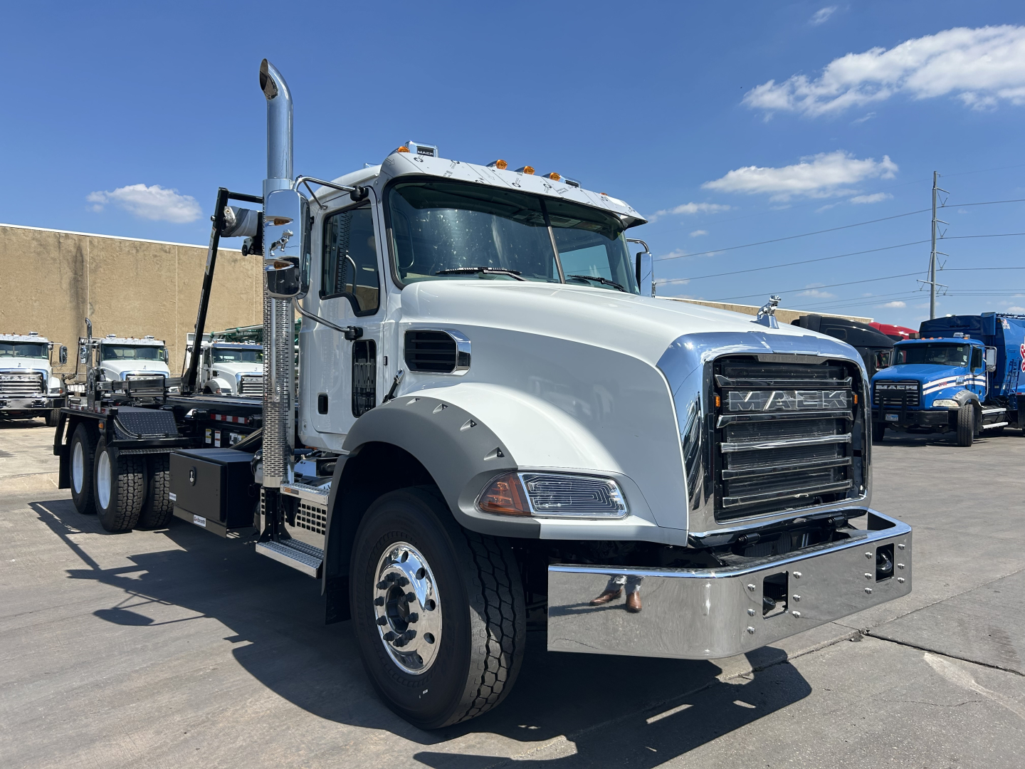 New 2026 Mack GR64B rolloff truck in white showing front grille, chrome bumper, oversized exhaust stack, and dual rear axles.