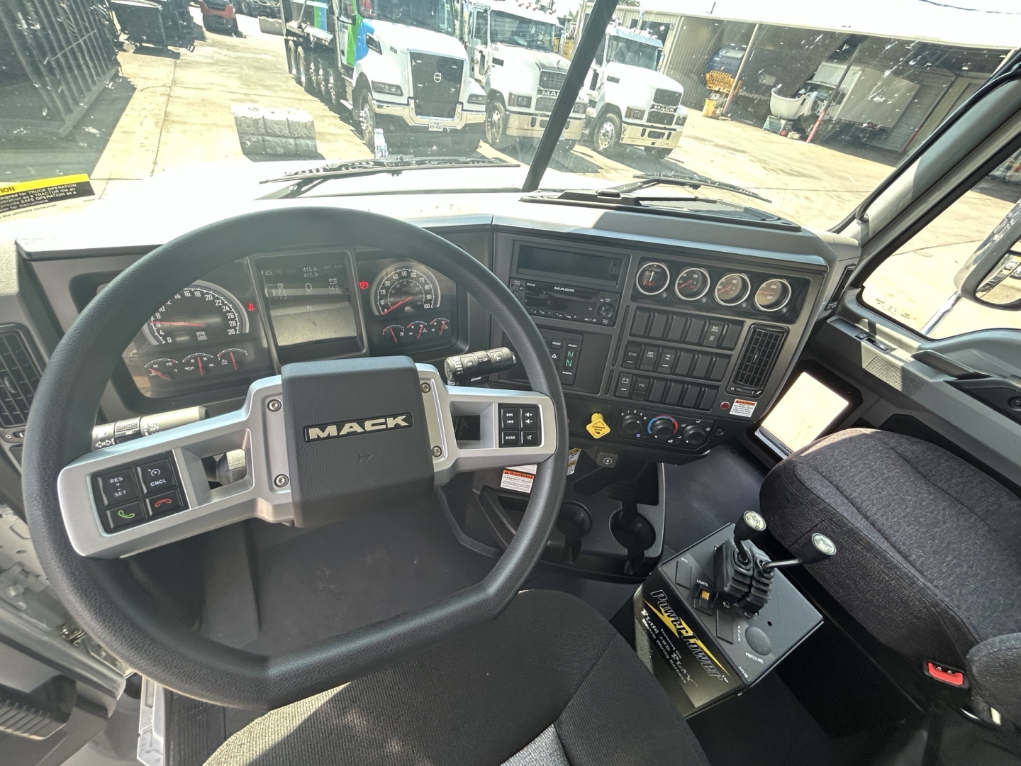 Mack GR64B truck cab interior showing steering wheel with MACk logo, dashboard gauges, console, and gear shifter in view.