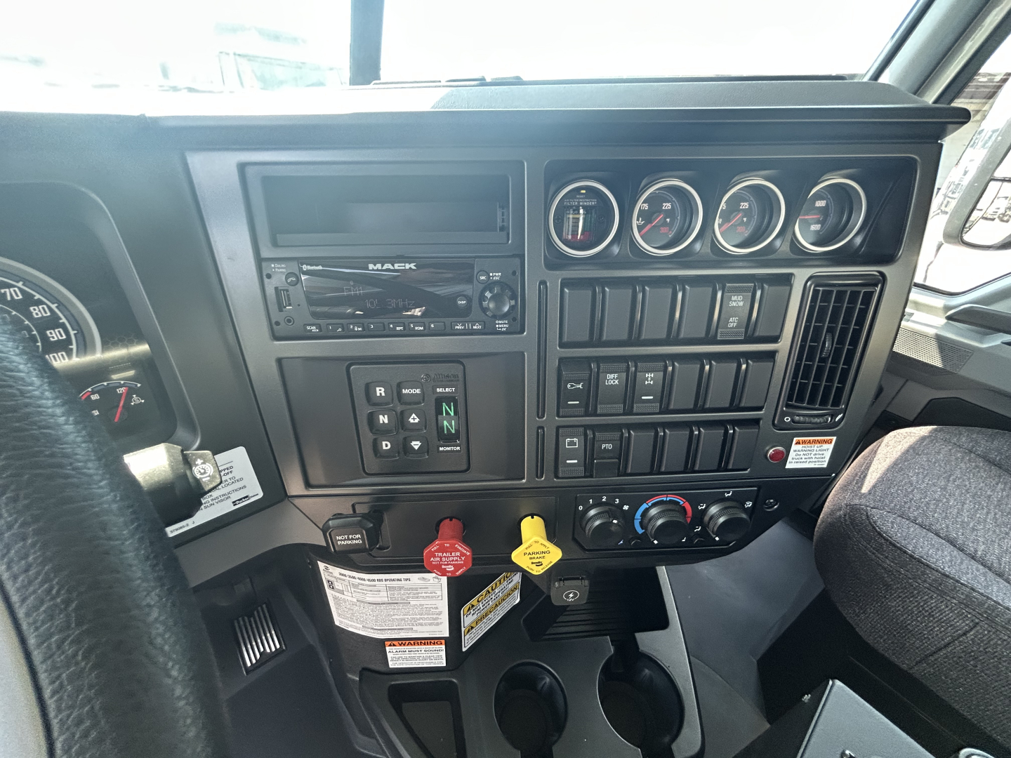 Dashboard of a 2026 Mack GR64B showing instrument cluster, radio, switches, and steering wheel.