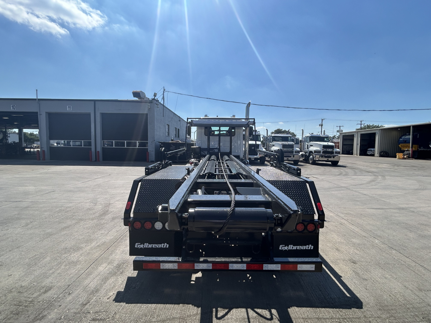 Flatbed tow truck chassis with loading ramps and tool compartments, view from rear showing dual rear taillights and platform edges.