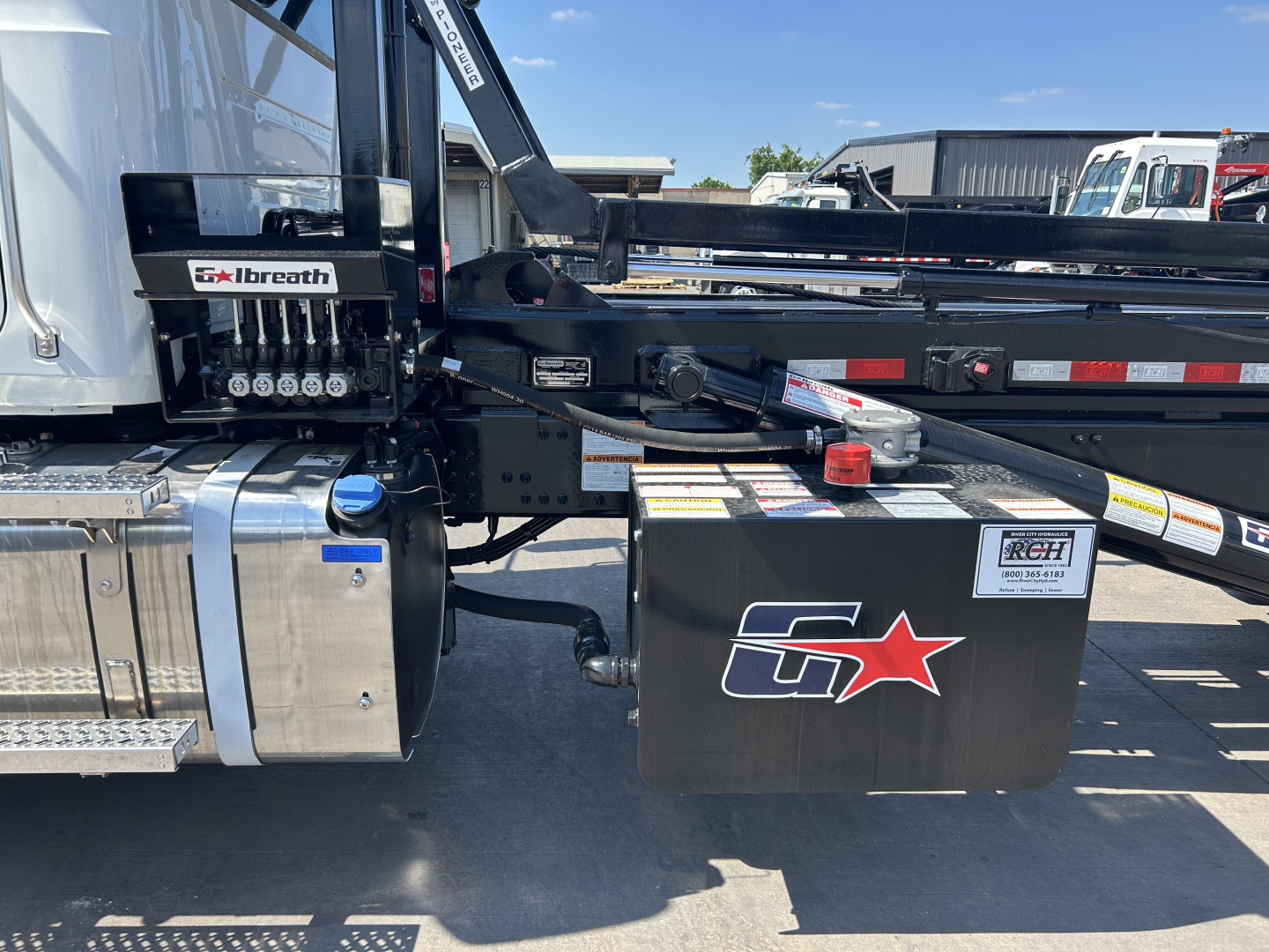 Truck hitch area of a 2026 Mack GR64B rolloff showing fuel tank, hydraulic valves labeled 'Sbreath' or similar, black tool box with a red star logo, and rear chassis components.