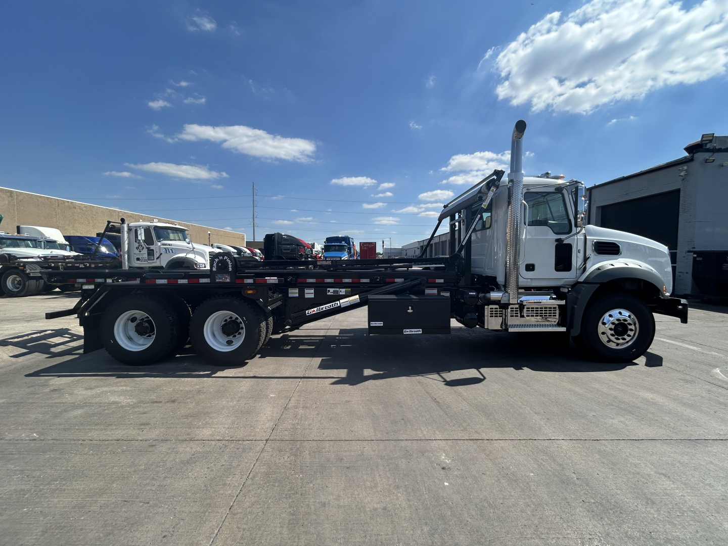Mack GR64B rolloff truck side view showing flatbed with dual rear axles and a crane/mole above cab area.