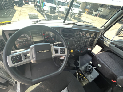 Mack GR64B truck cab interior showing steering wheel with MACk logo, dashboard gauges, console, and gear shifter in view.