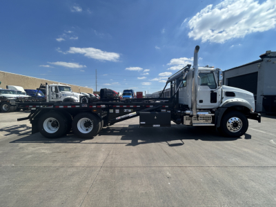 Mack GR64B rolloff truck side view showing flatbed with dual rear axles and a crane/mole above cab area.
