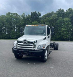 Hino L7 cab chassis truck front-left view with white cab and dual rear wheels, stock number H27004, new vehicle in lot.