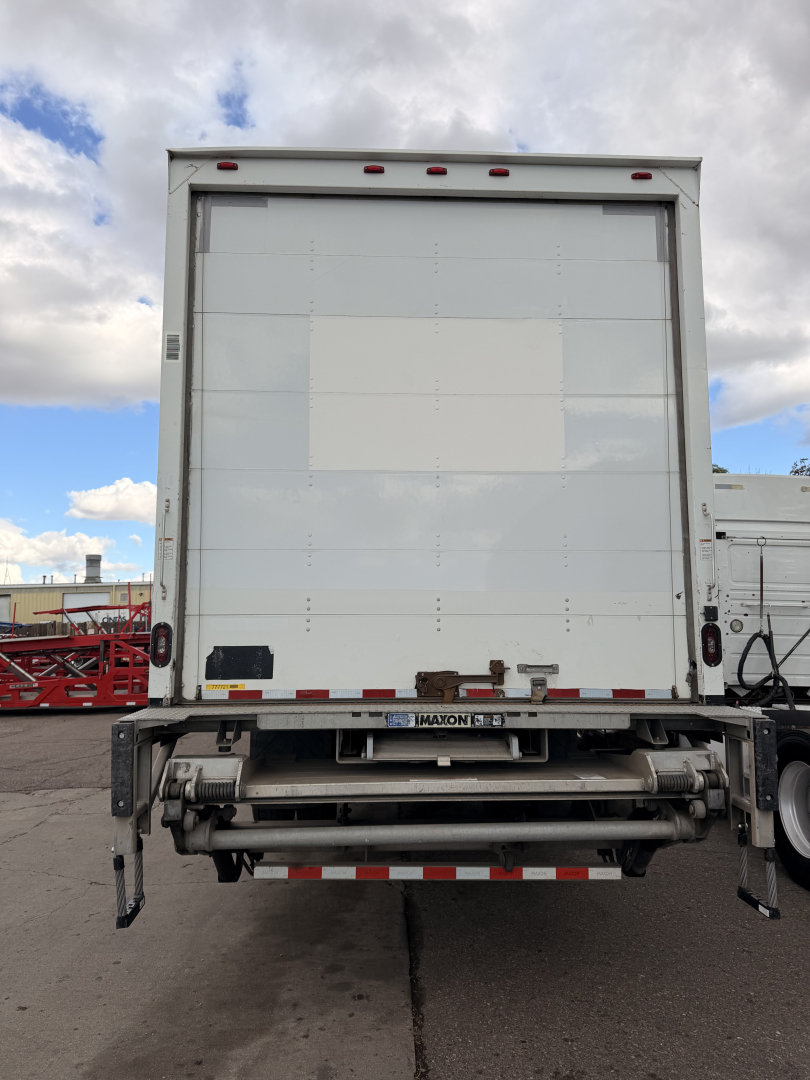 Rear view of 2018 Freightliner M2-106 box truck showing liftgate and closed cargo area. Visible text includes Maxon liftgate branding and reflective safety tape along bottom edge.