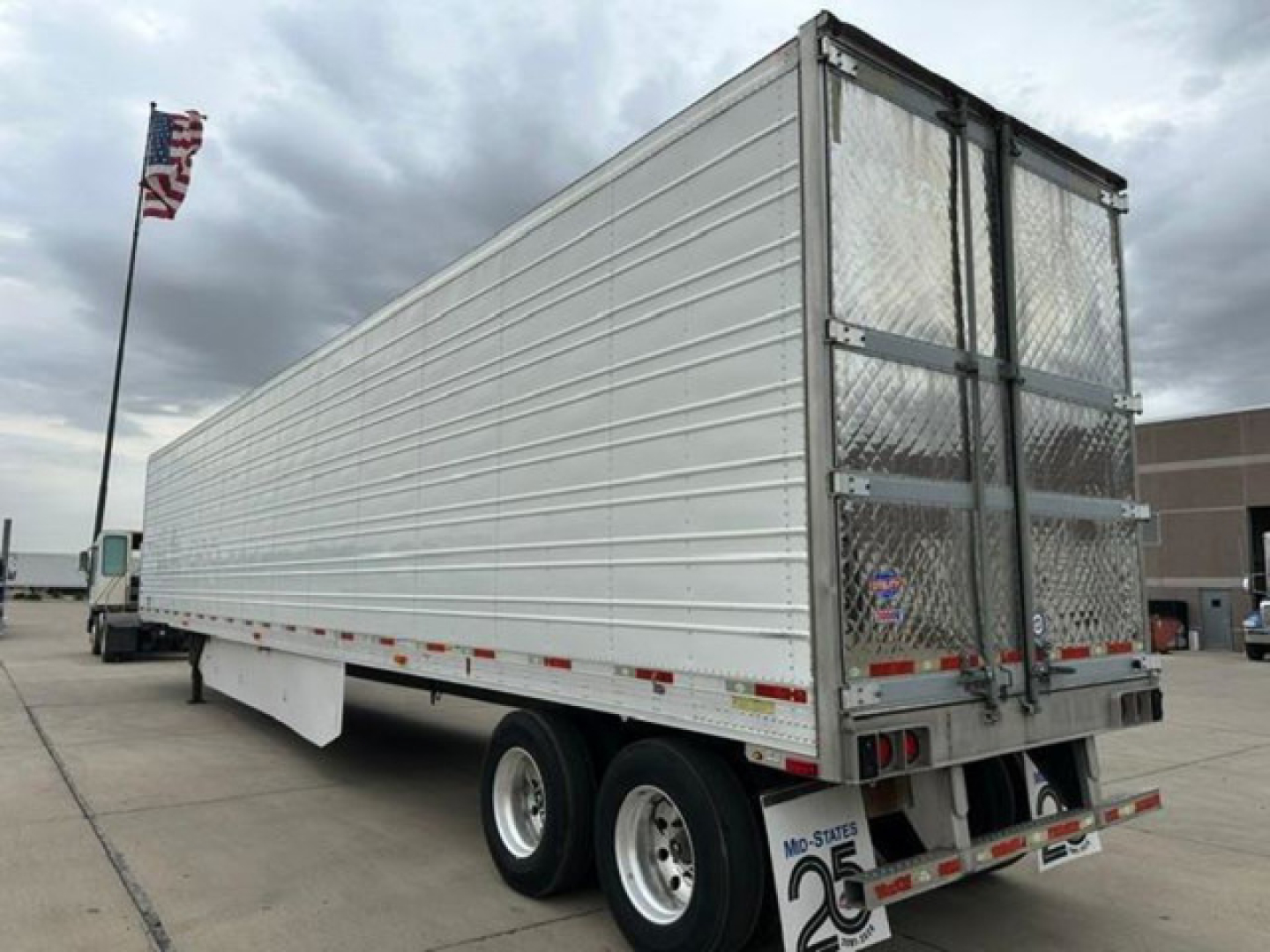 Trailer side view of a 2016 utility reefer with metal siding and rear doors, dual rear axles, and diamond plate gate.
