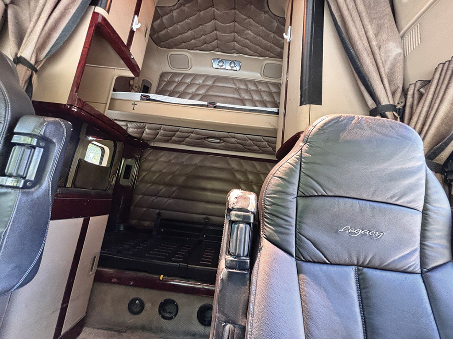 Truck cabin interior of a 2015 Freightliner Coronado showing sleeper berth area with padded bed, curtains, and leather seats.