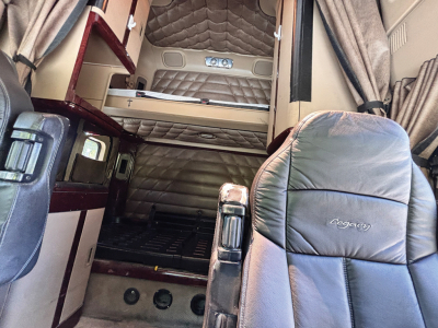 Truck cabin interior of a 2015 Freightliner Coronado showing sleeper berth area with padded bed, curtains, and leather seats.
