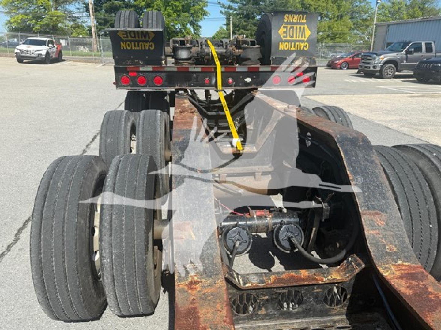 ETNYRE beam lowboy trailer rear view showing dual rear axles with six wheels, rusted steel frame, and hydraulic lines; warning straps on top and clearance lights.